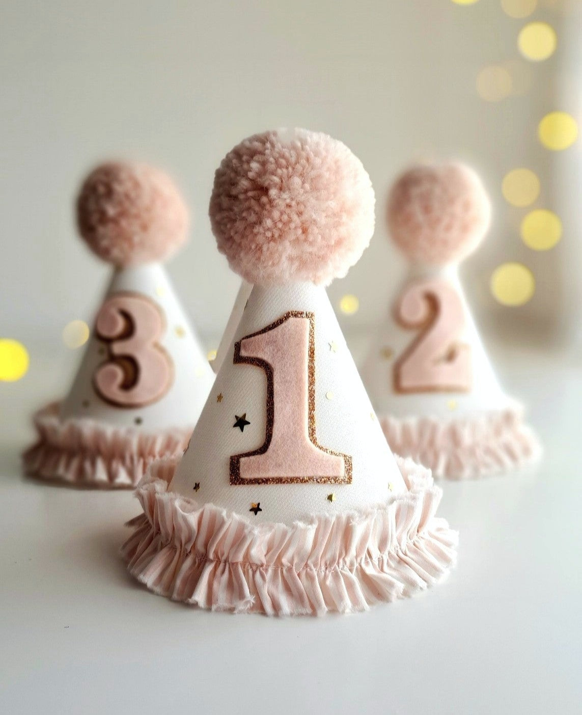 Detailed shot of tulle, linen, and cotton textures on pink birthday party hats showing felt numbers