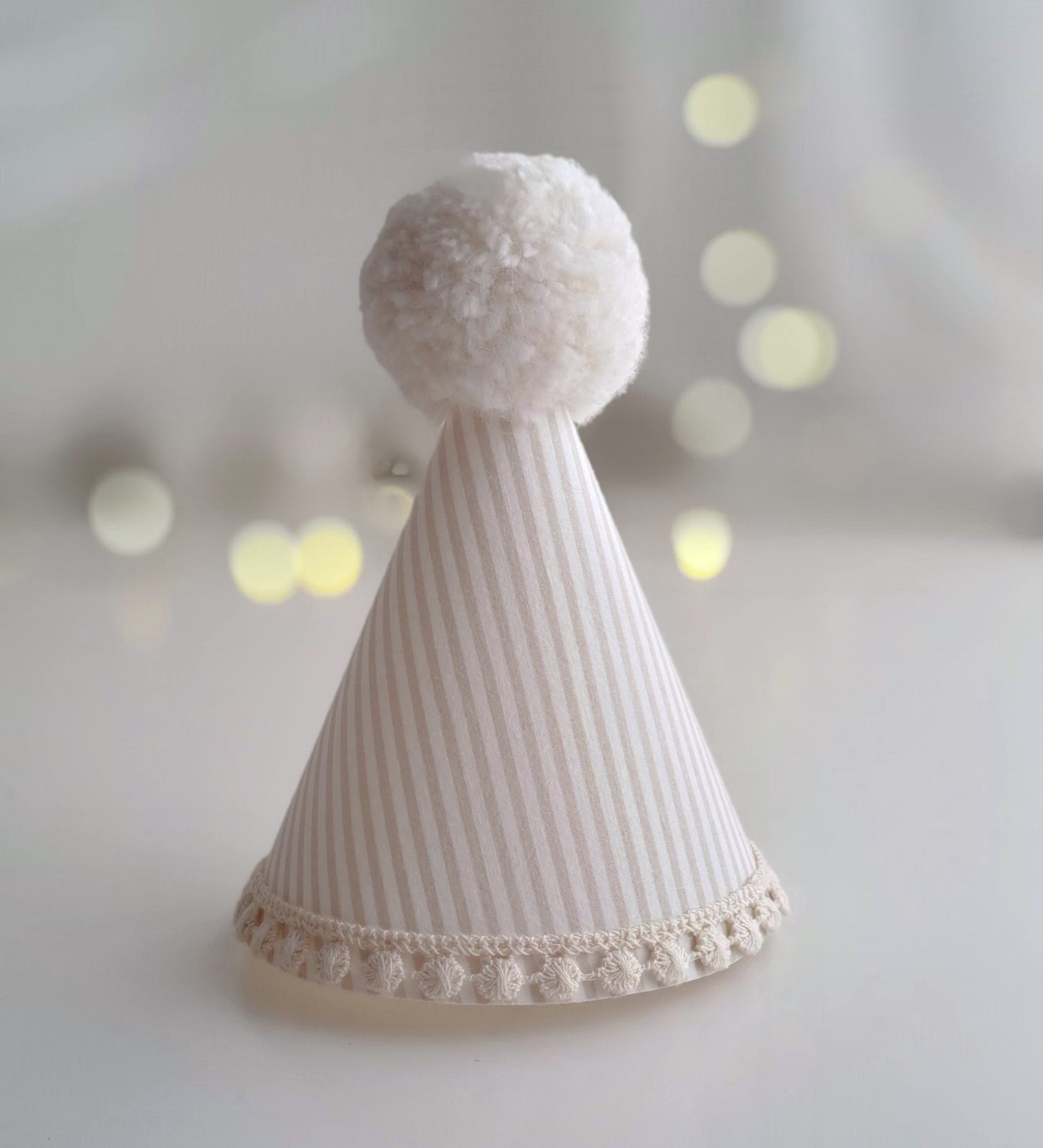 A caramel and cream stripe party hat. The hat has a cream crochet trim at the bottom and a lovely fluffy pompom on top by Verity Isabelle.