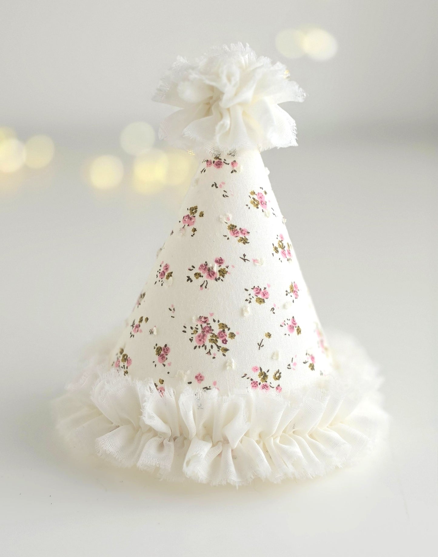 Ditsy floral handmade birthday party hat in ivory fabric with pink roses and white ruffle trim, By Verity Isabelle.