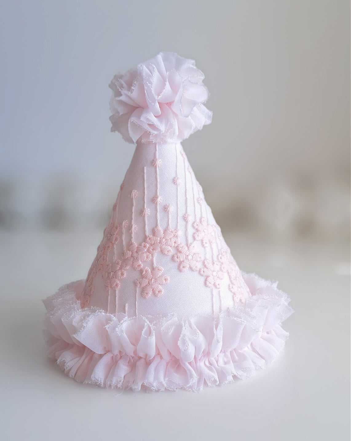 Soft pink princess party hat with embroidered floral lace fabric, white ruffle trim and fabric pom pom, handmade by Verity Isabelle.
