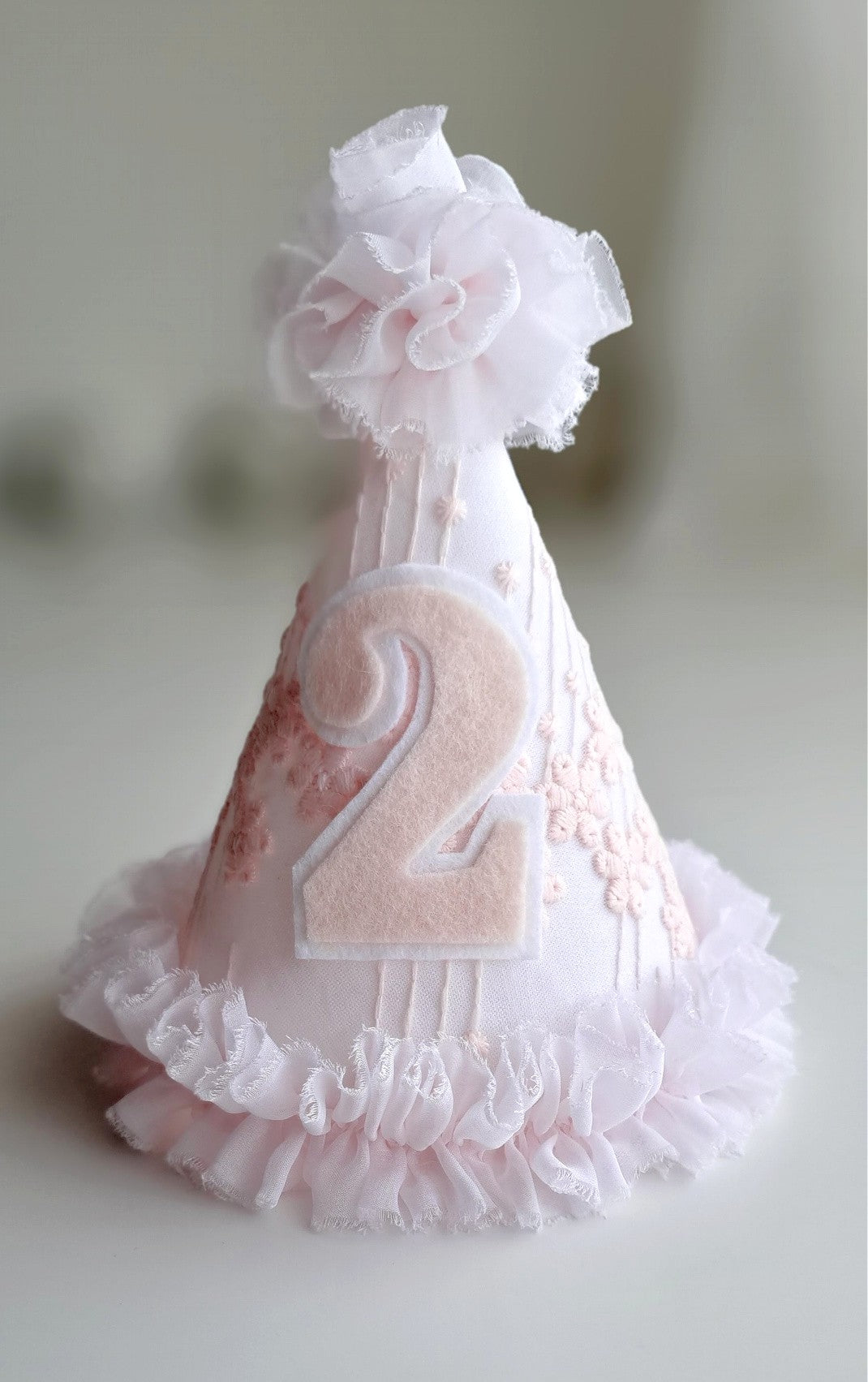 Soft pink number 2 birthday party hat with embroidered lace detail, felt number and white ruffle trim, handmade by Verity Isabelle.