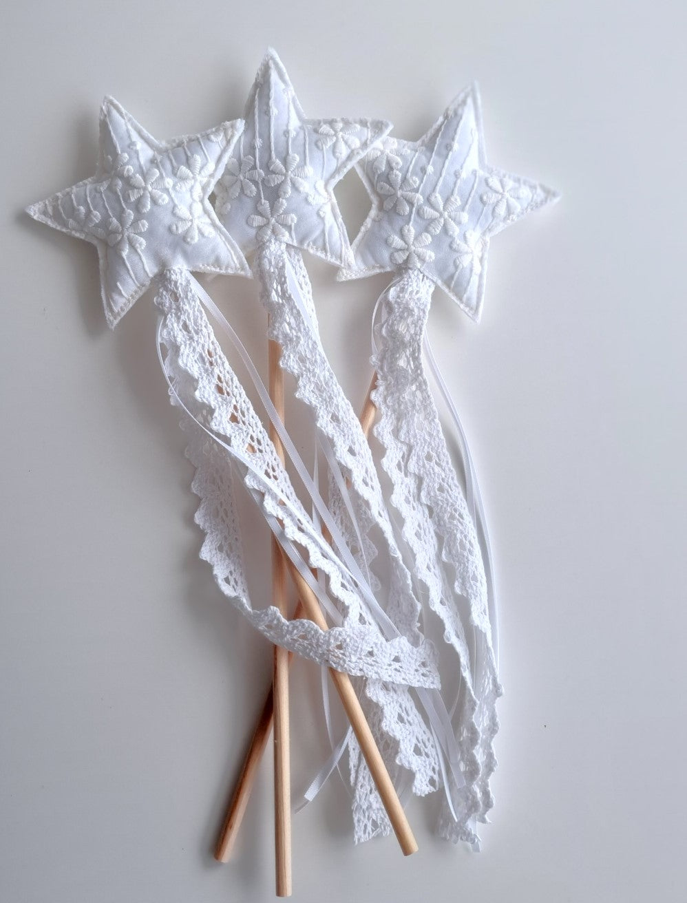 Group of white floral lace star wands with white satin ribbon and cotton lace streamers flowing from a solid wood stick handle.  By Verity Isabelle.