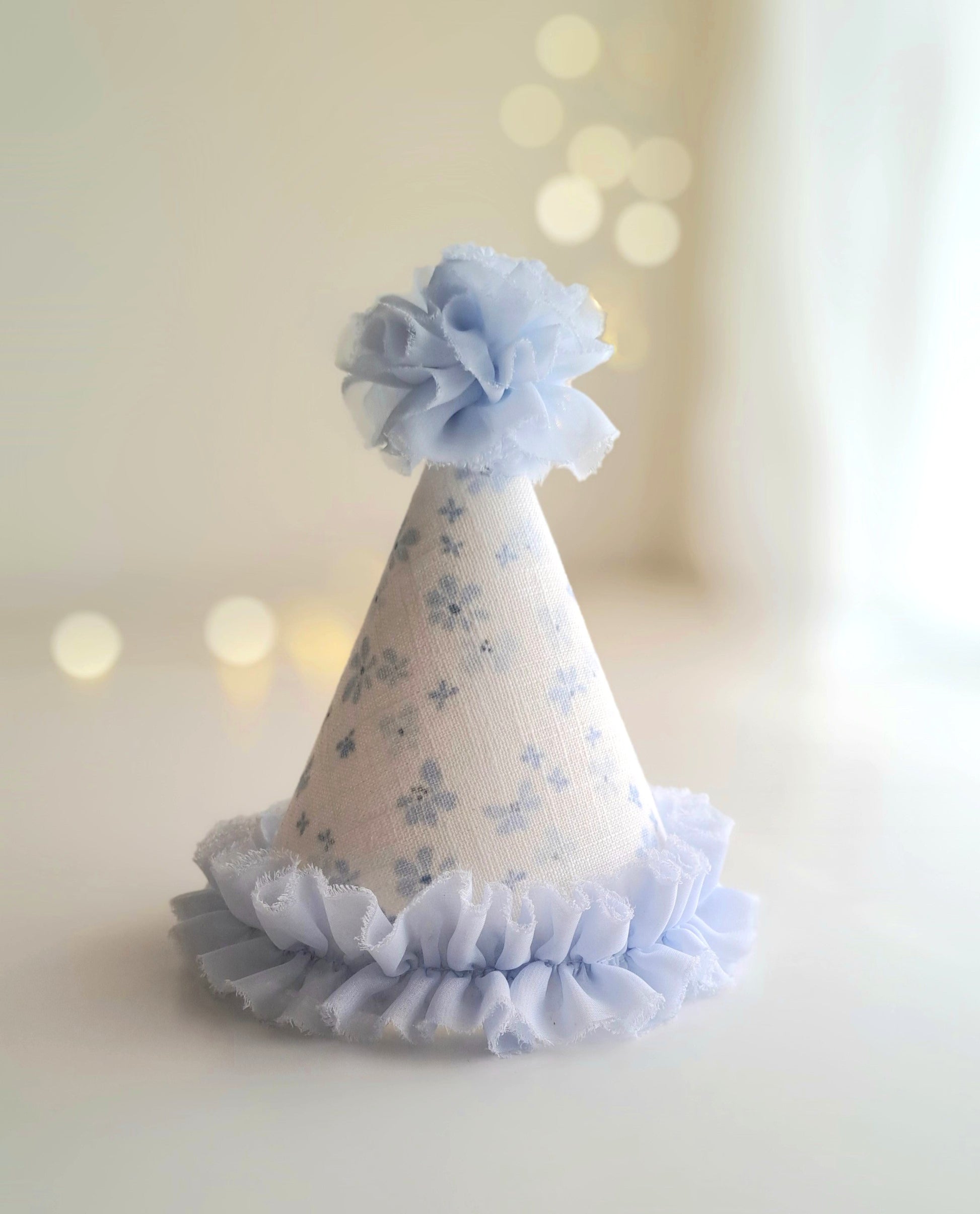 Plain blue floral linen party hat with soft fabric pom pom and pale blue ruffle trim, handmade by Verity Isabelle.