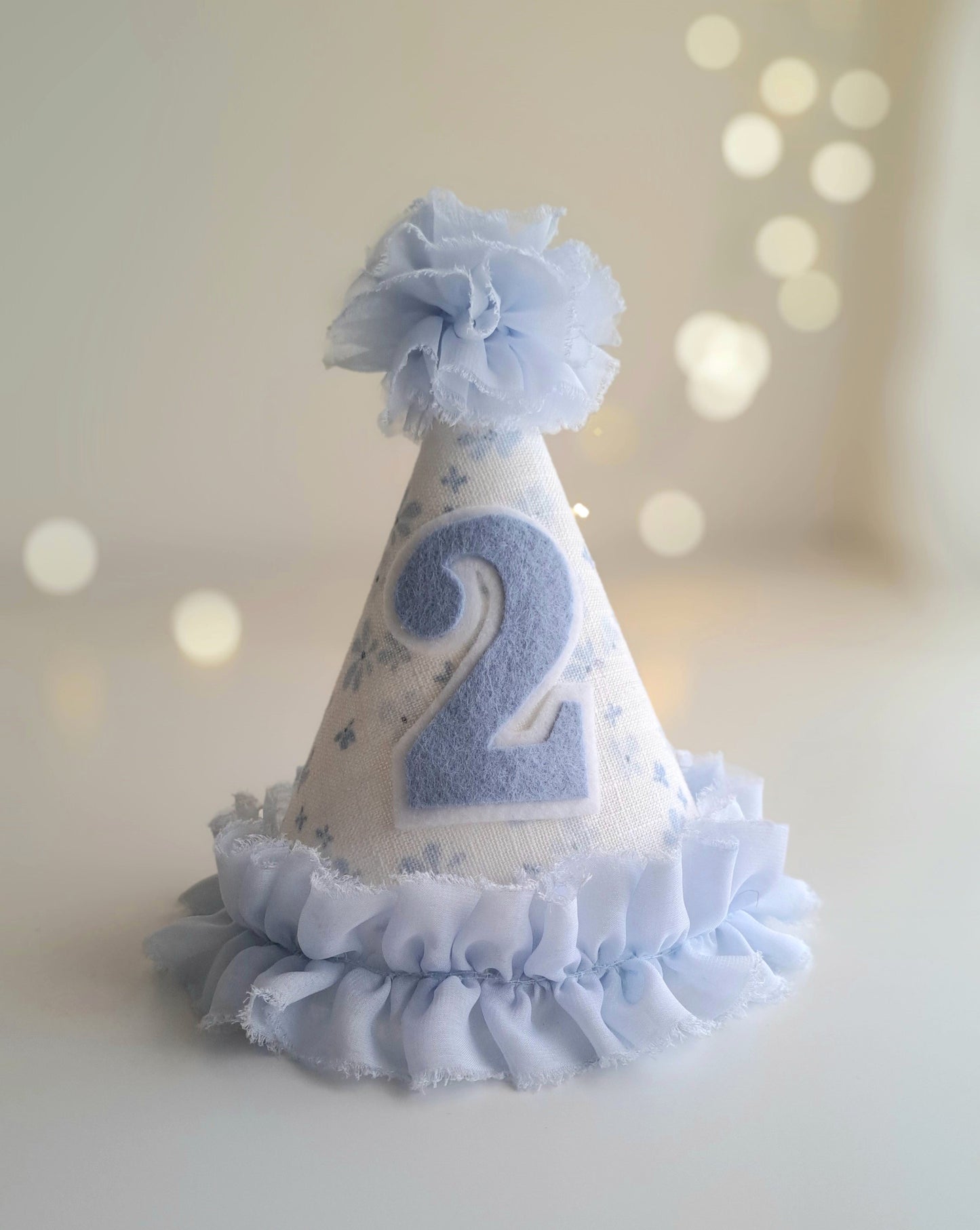 Blue number 2 birthday party hat with floral fabric, soft blue felt number, fabric pom pom and ruffle trim.