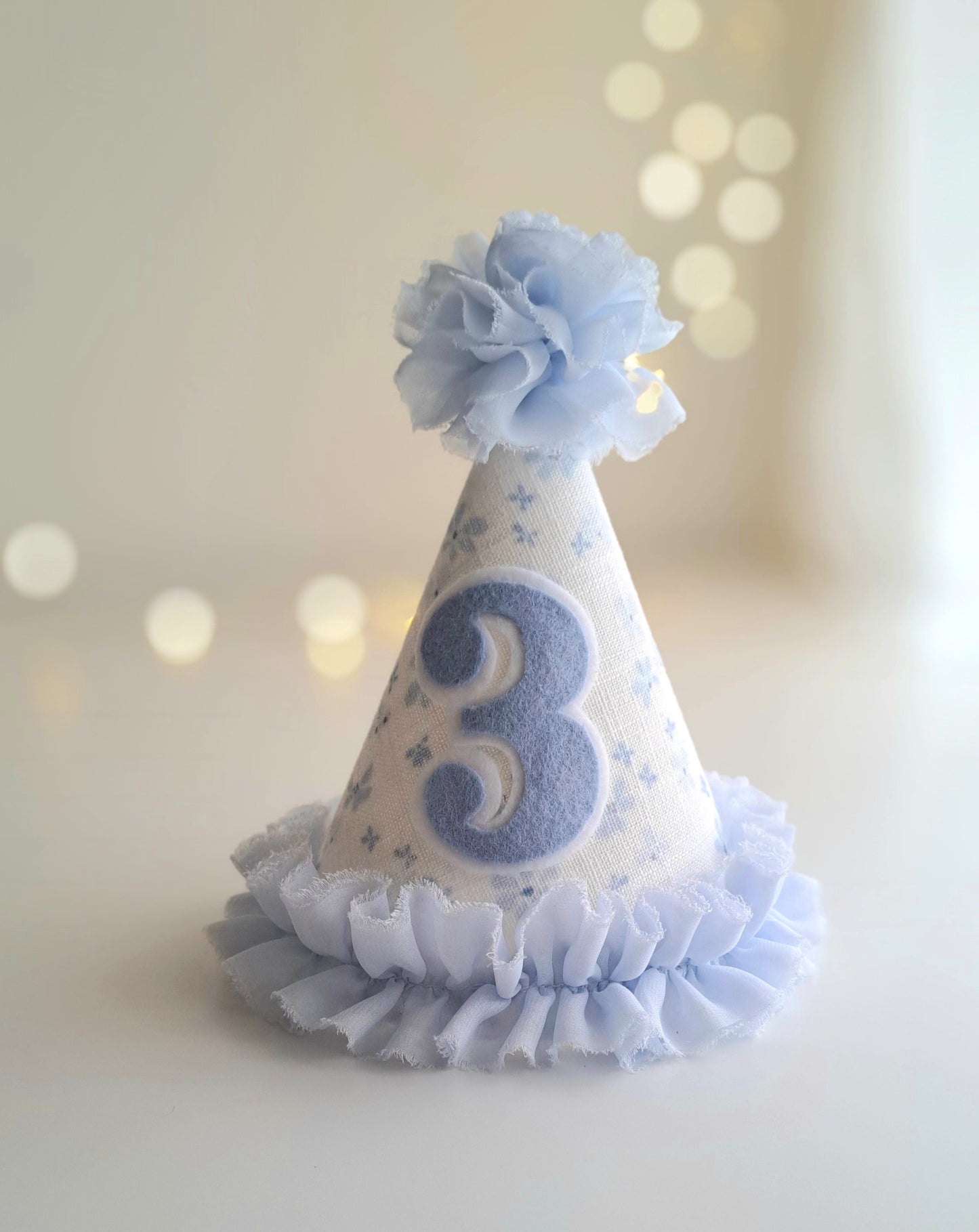 Blue number 3 birthday party hat with floral fabric, soft blue felt number, fabric pom pom and ruffle trim.