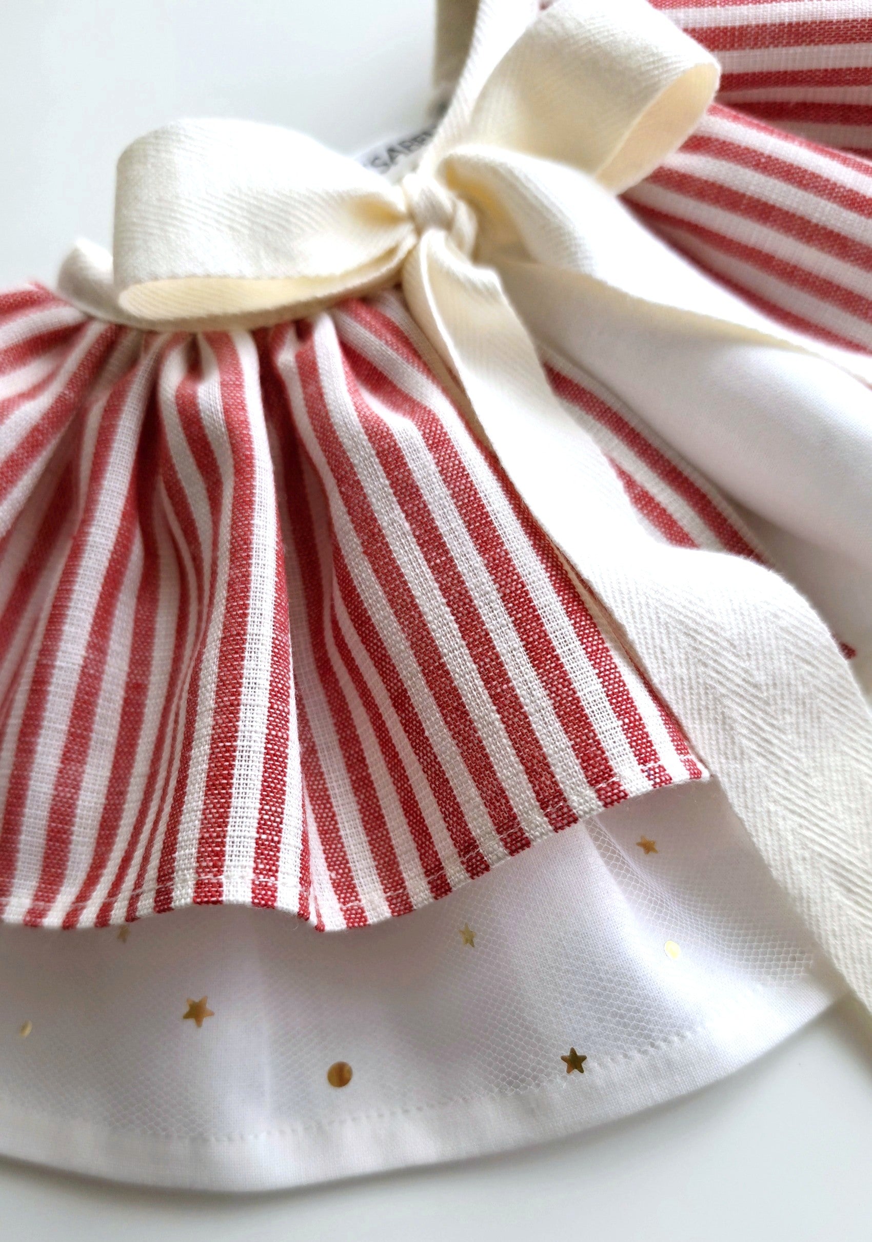 Close up of handmade circus cape showing red stripe fabric, ivory bow tie and star tulle layer