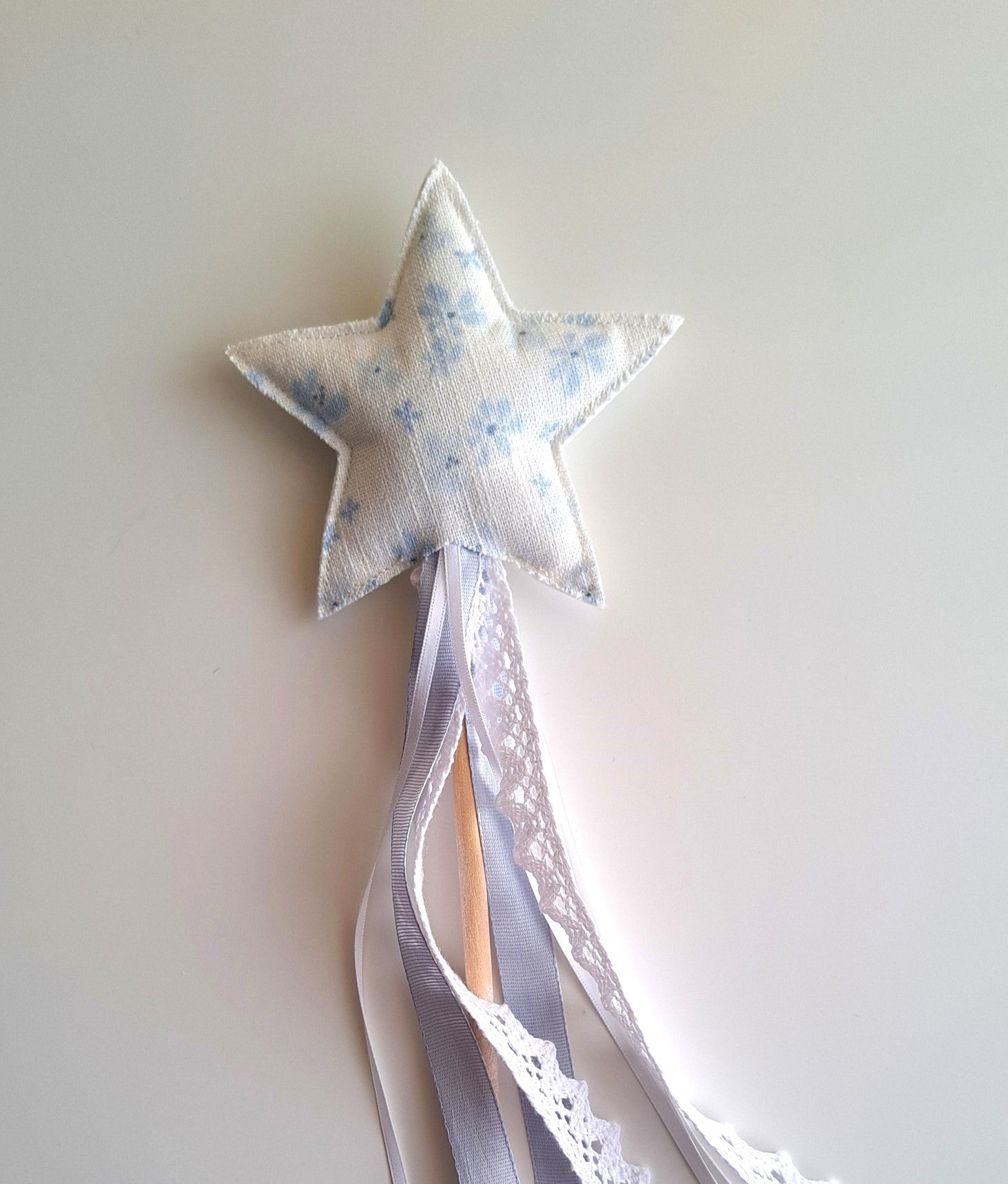 Close-up of a handmade blue floral star wand with fabric star, wooden handle, lace trim and soft ribbon streamers.