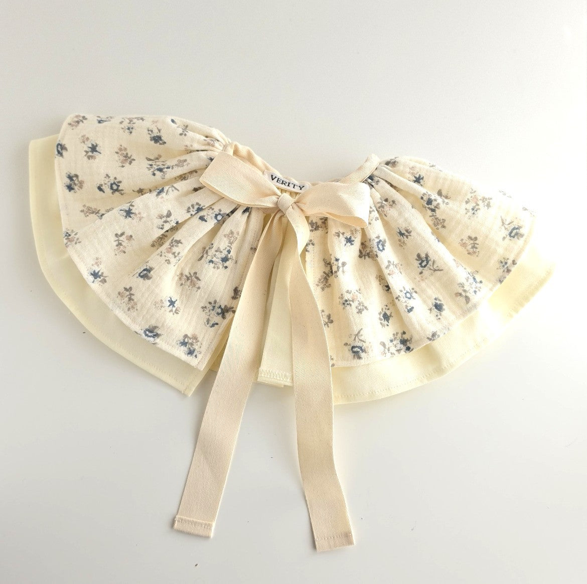 Handmade Mabel floral party cape in pale lemon fabric with blue ditsy floral print, soft cotton lining and ribbon ties.