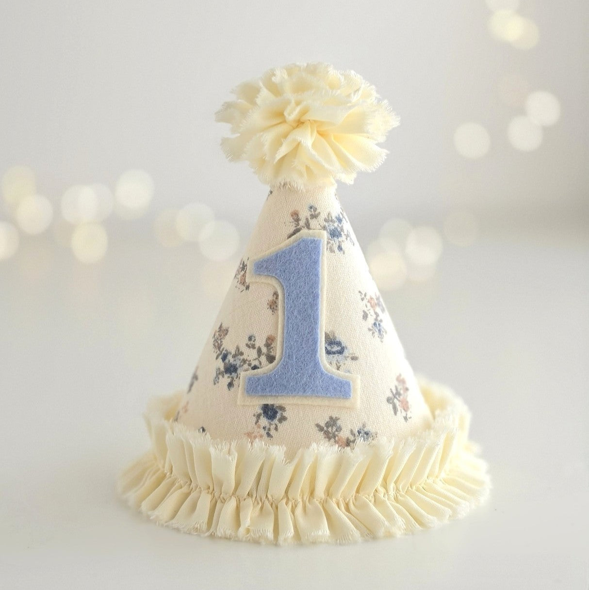Handmade Mabel floral first birthday party hat in pale lemon linen with blue ditsy floral print, soft ruffle trim and blue number one applique.