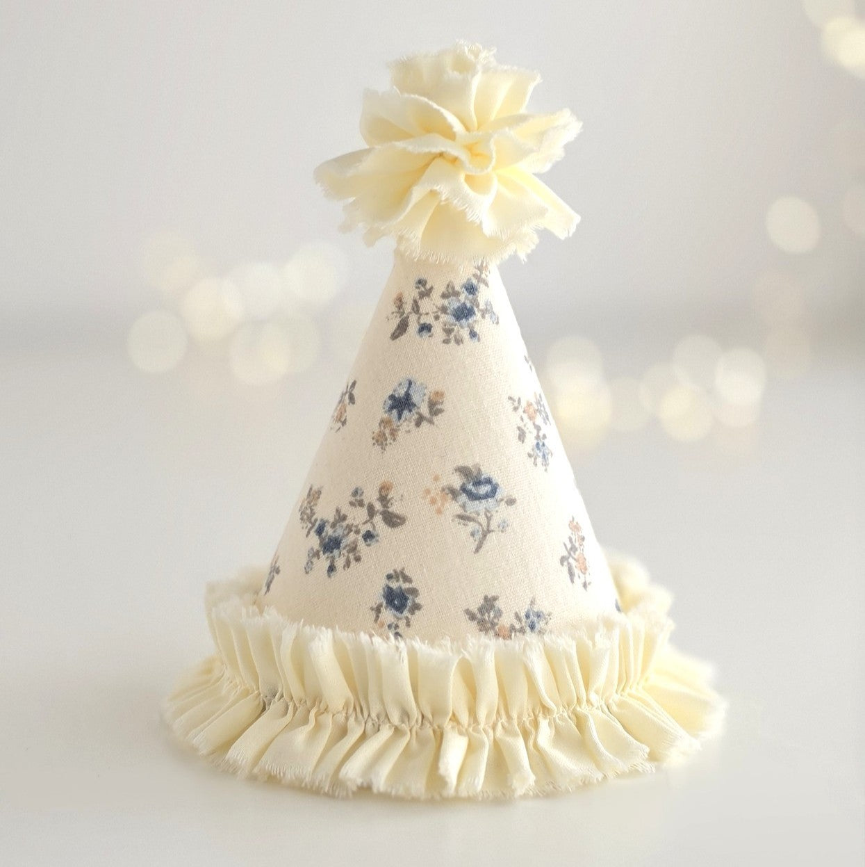 Handmade Mabel floral party hat in pale buttery lemon fabric with delicate blue ditsy floral print and soft gathered ruffle trim.