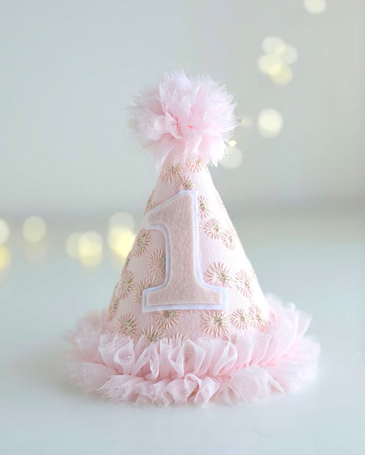 Pink Starburst first birthday party hat with felt number 1, pale pink embroidered lace, gold starburst detail, chiffon ruffle trim and pom-pom. By Verity Isabelle.