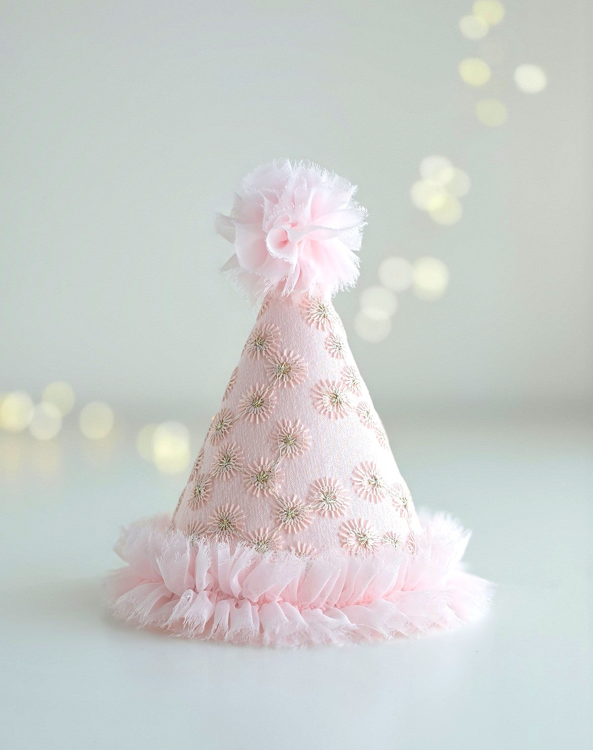 Plain Pink Starburst birthday party hat made from pale pink embroidered lace with gold starburst detail, chiffon ruffle trim and pom-pom. By Verity Isabelle.