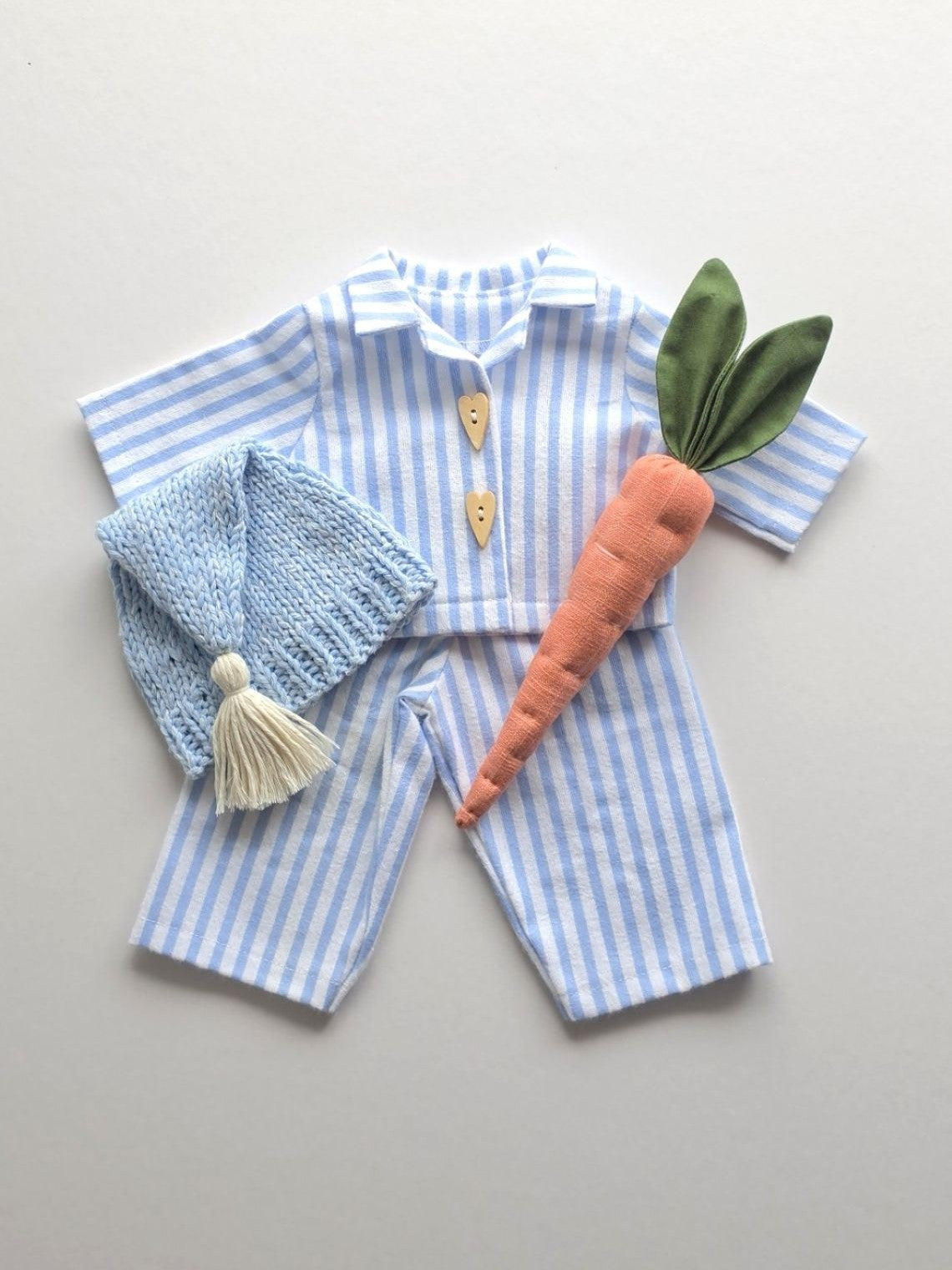 Blue striped bunny pyjama outfit with knitted sleepy hat and handmade linen carrot, shown as a flat lay.