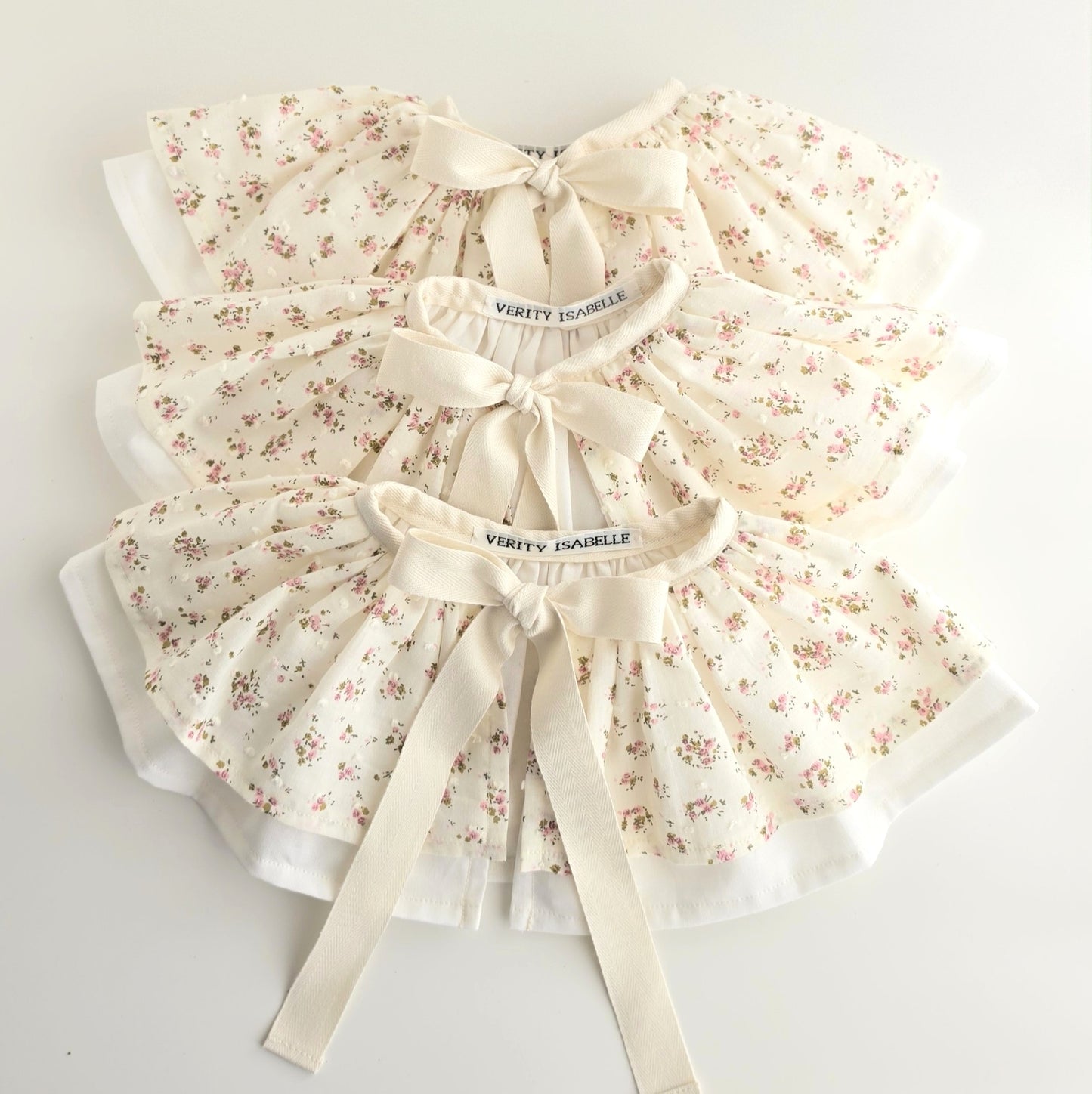 Ditsy floral birthday capes in ivory fabric with pink roses, white cotton lining and cream herringbone twill bow ties.