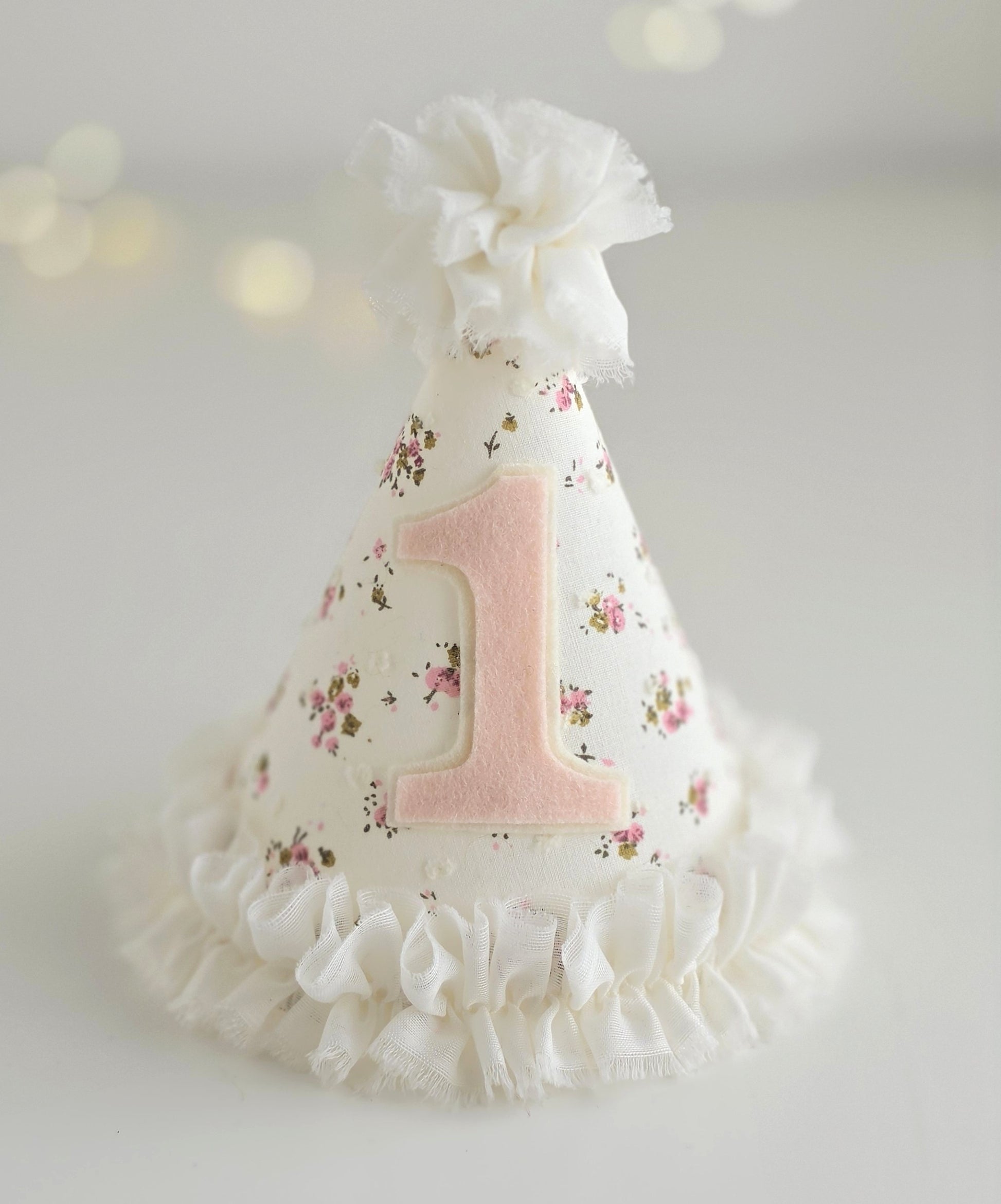 Ditsy floral first birthday party hat with pale pink number 1 and white chiffon ruffle trim and pompom on top.