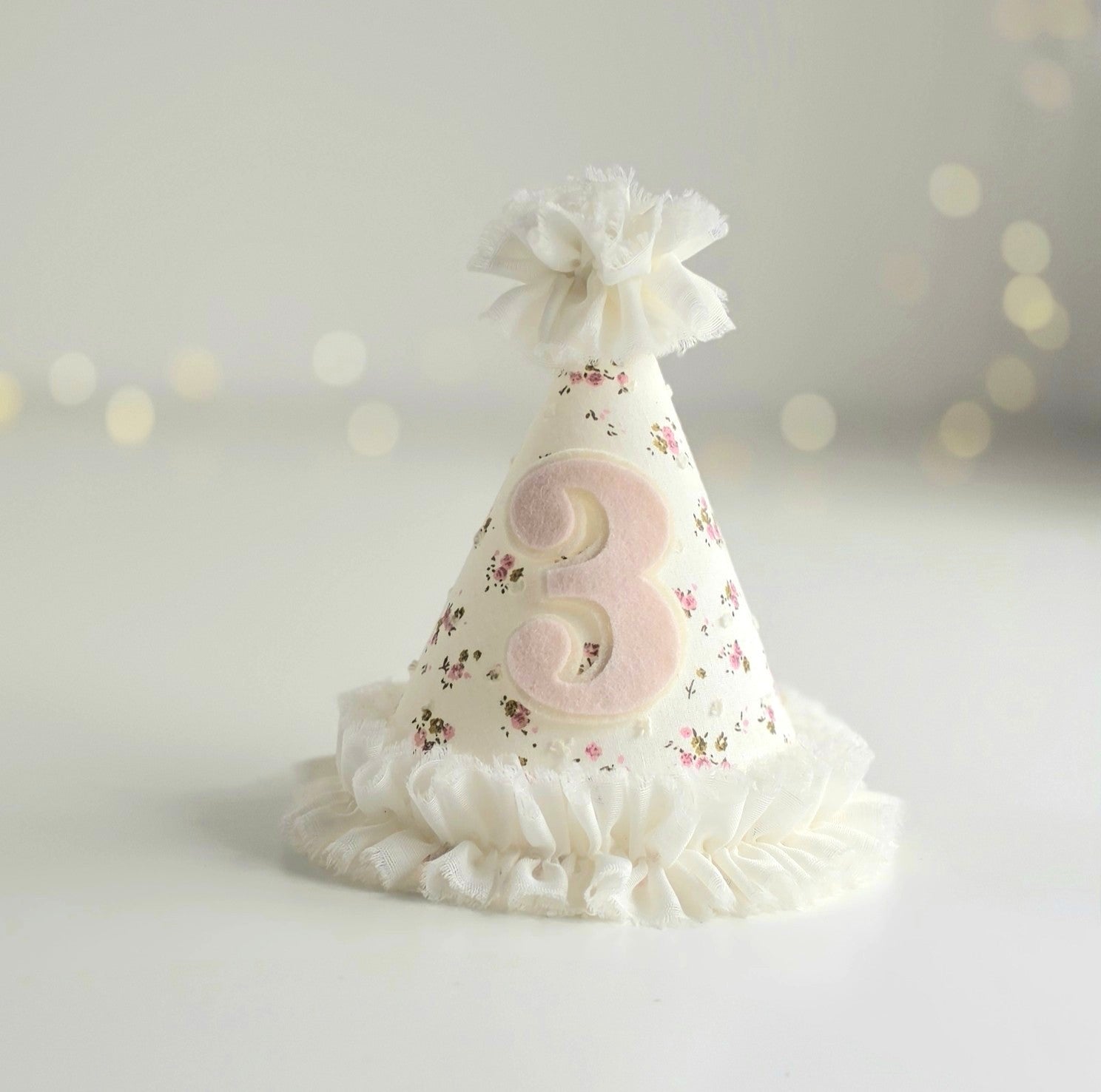 Ditsy floral third birthday party hat with pale pink felt number 3 and white chiffon ruffle trim, with matching pompom.