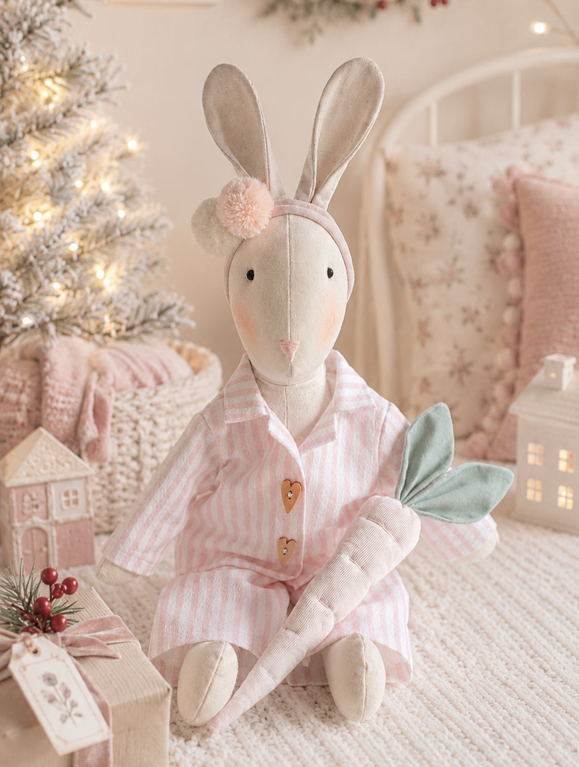 Handmade Veronica Bunny in pink striped Christmas pyjamas holding a pink linen carrot beside a softly lit Christmas tree.
