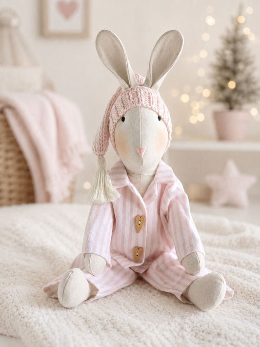 Handmade linen Veronica Bunny in pink striped pyjamas and knitted sleepy hat, with soft Christmas lights and tree.