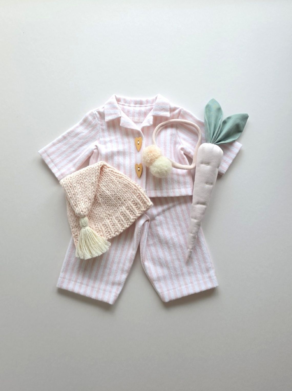 Pink striped bunny pyjama outfit with knitted sleepy hat and handmade linen carrot, shown as a flat lay.