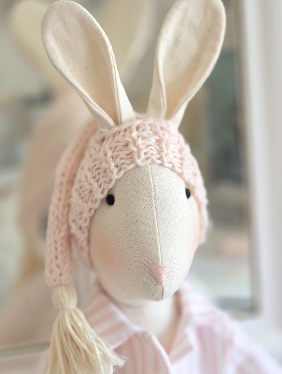 Close-up of handmade linen Veronica Bunny wearing a pale pink knitted sleepy hat and pink striped pyjamas.
