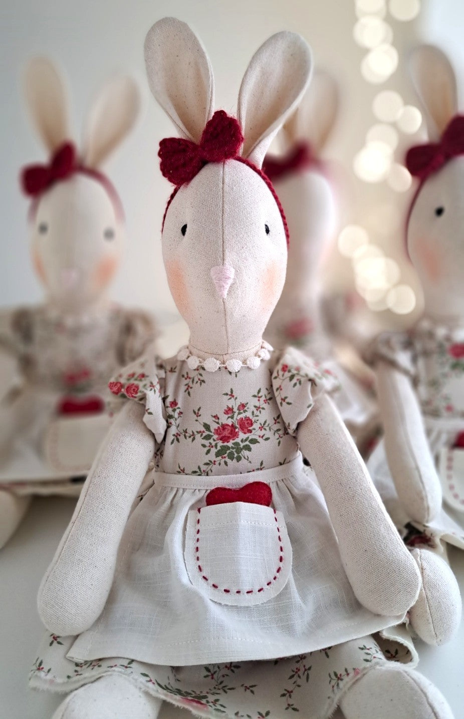 Handmade Valentine’s Veronica Bunny sitting softly, wearing a floral cotton dress, linen apron and red felt heart, a timeless keepsake toy