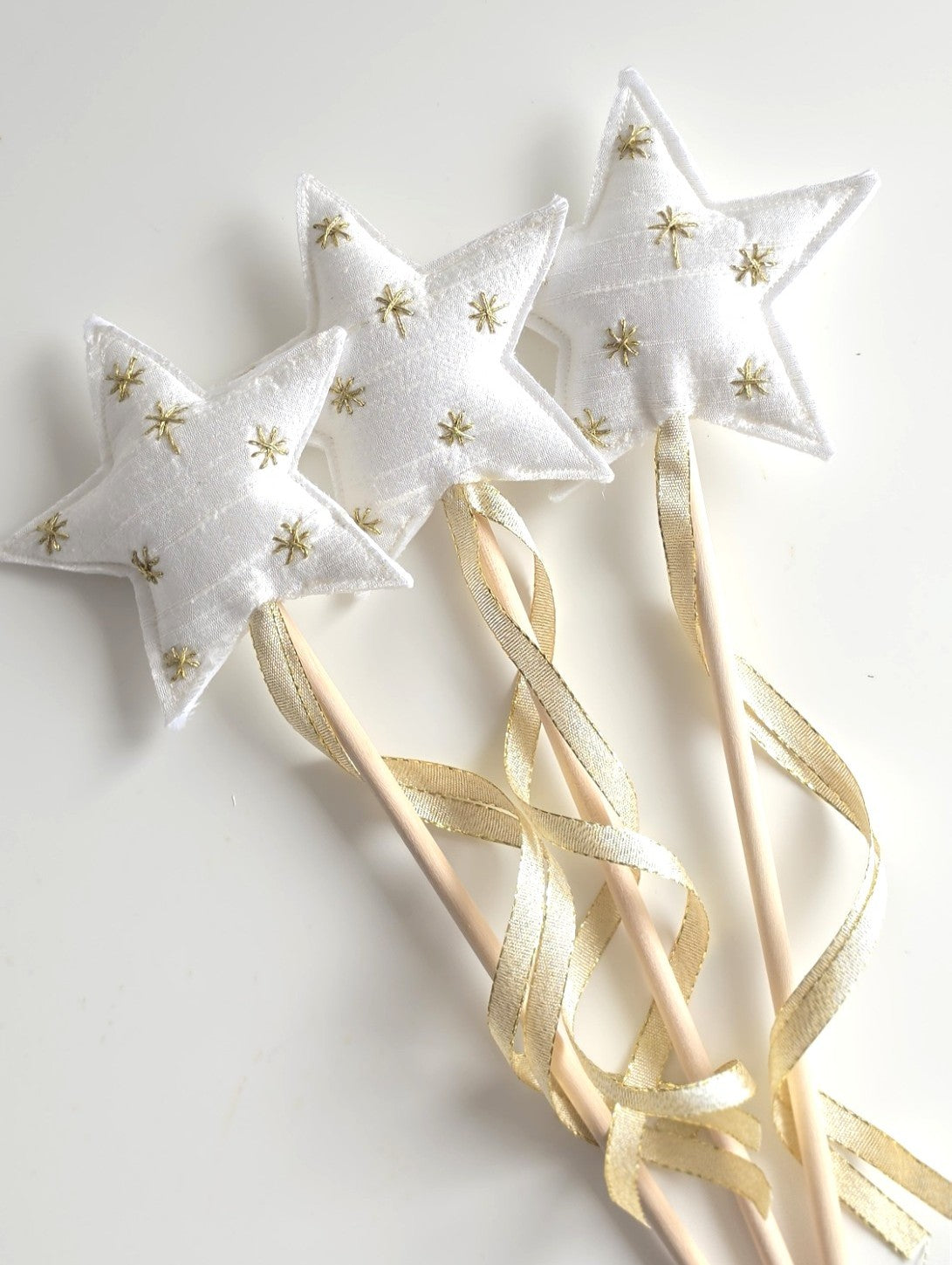 Three white silk Christmas star wands with gold embroidered stars, wooden handles and trailing gold ribbon.