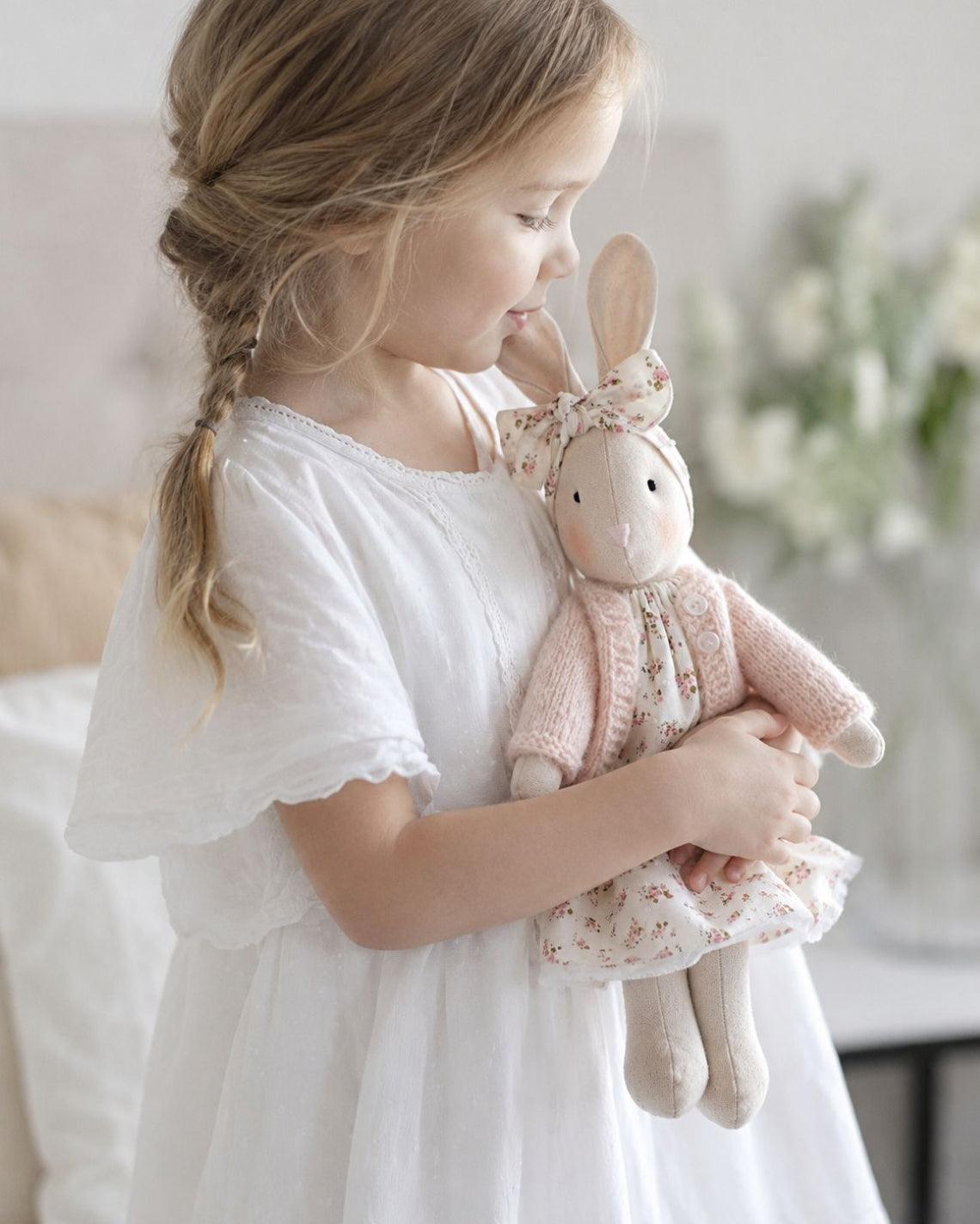 Young girl holding a pink bunny stuffed toy in a softly lit room.