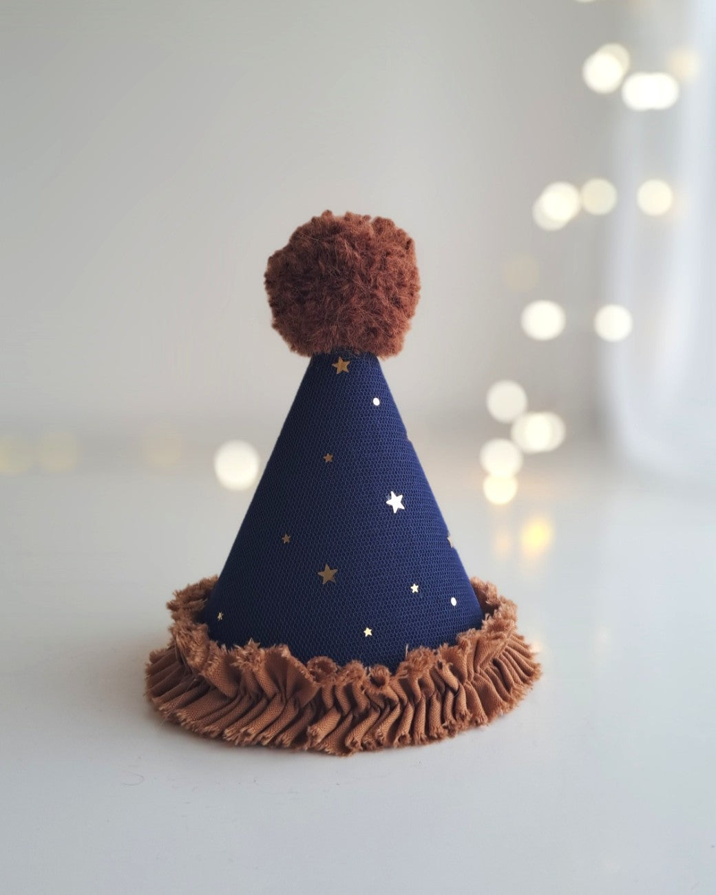 Handmade midnight navy linen party hat with gold star tulle overlay, finished with a soft ginger alpaca pom-pom and cotton ruffle trim.