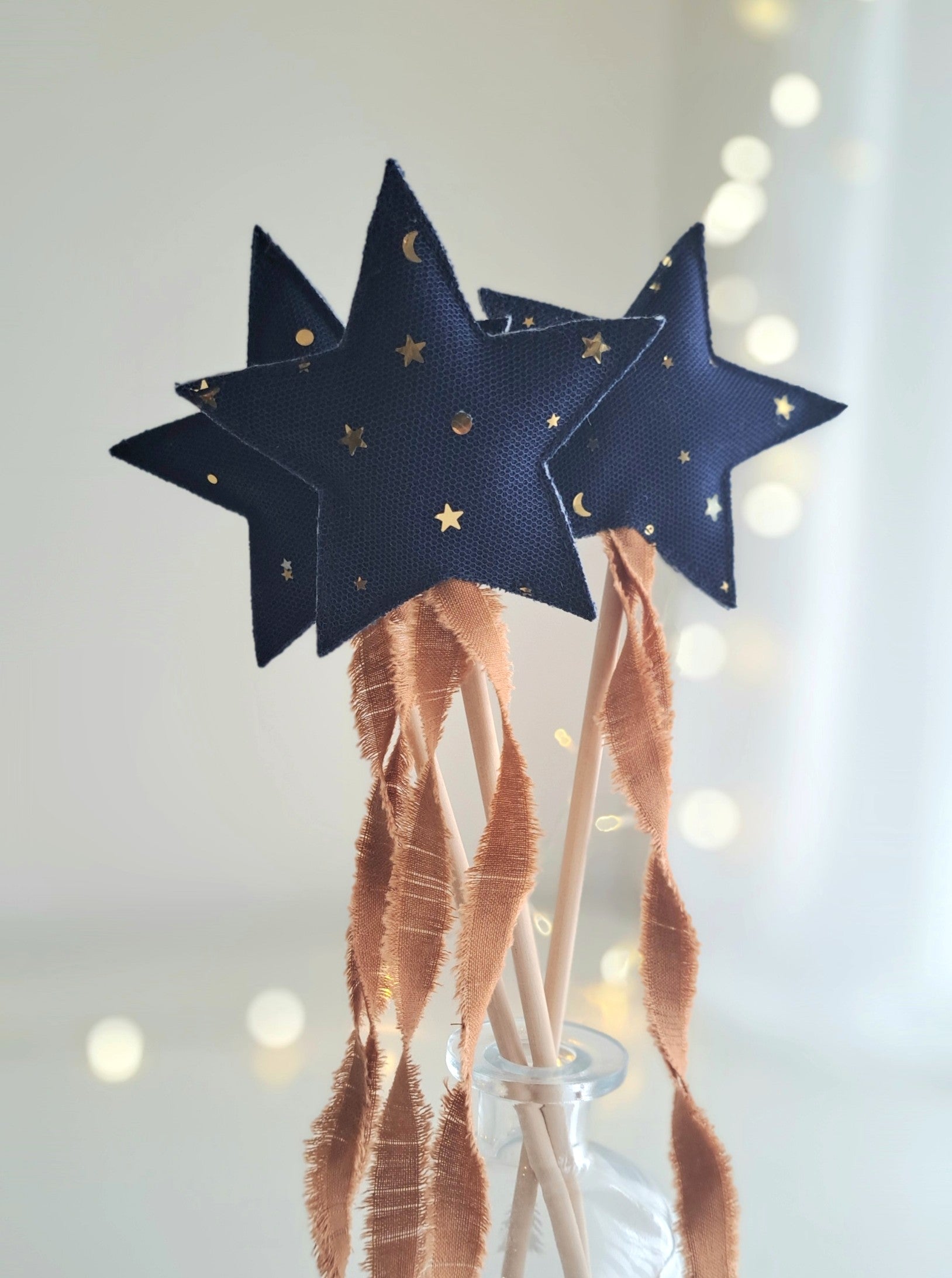 Set of three handmade star wands crafted from navy linen with gold star tulle overlay and frayed ginger cotton ribbon streamers on wooden sticks.