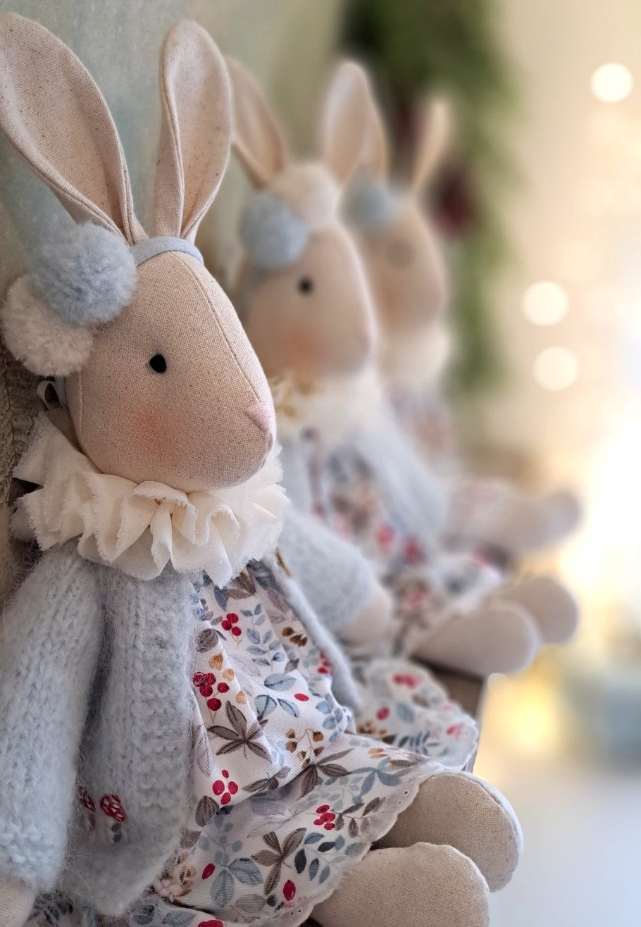 Three plush bunny toys in knitted and floral dresses against a blurred background